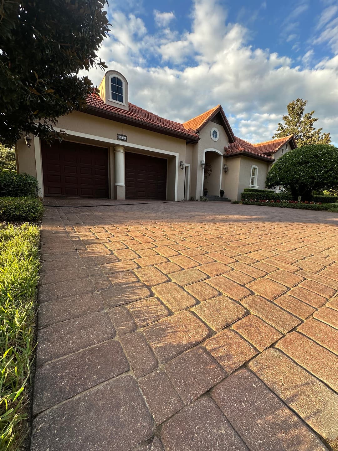 Elegant house with a red tile roof, two garage doors, and a landscaped driveway under blue sky.