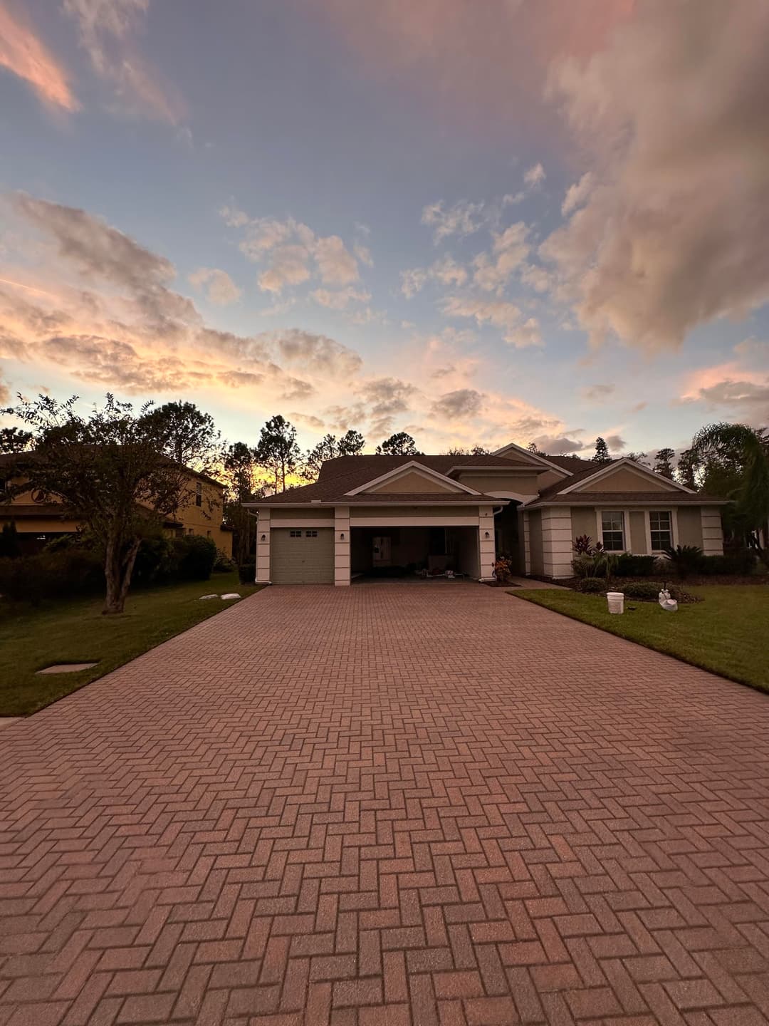 Modern house with landscaped yard and sunset sky, featuring a paver driveway and garage.