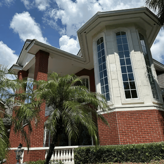 Luxury red brick house with large windows and palm trees under a blue sky.
