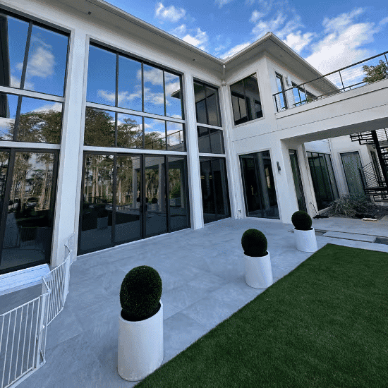 Modern luxury home exterior with large windows, spacious patio, and manicured landscaping.