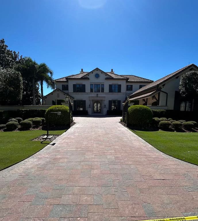 Elegant two-story mansion with landscaped front yard and clear blue sky. Paved walkway leading to entrance.