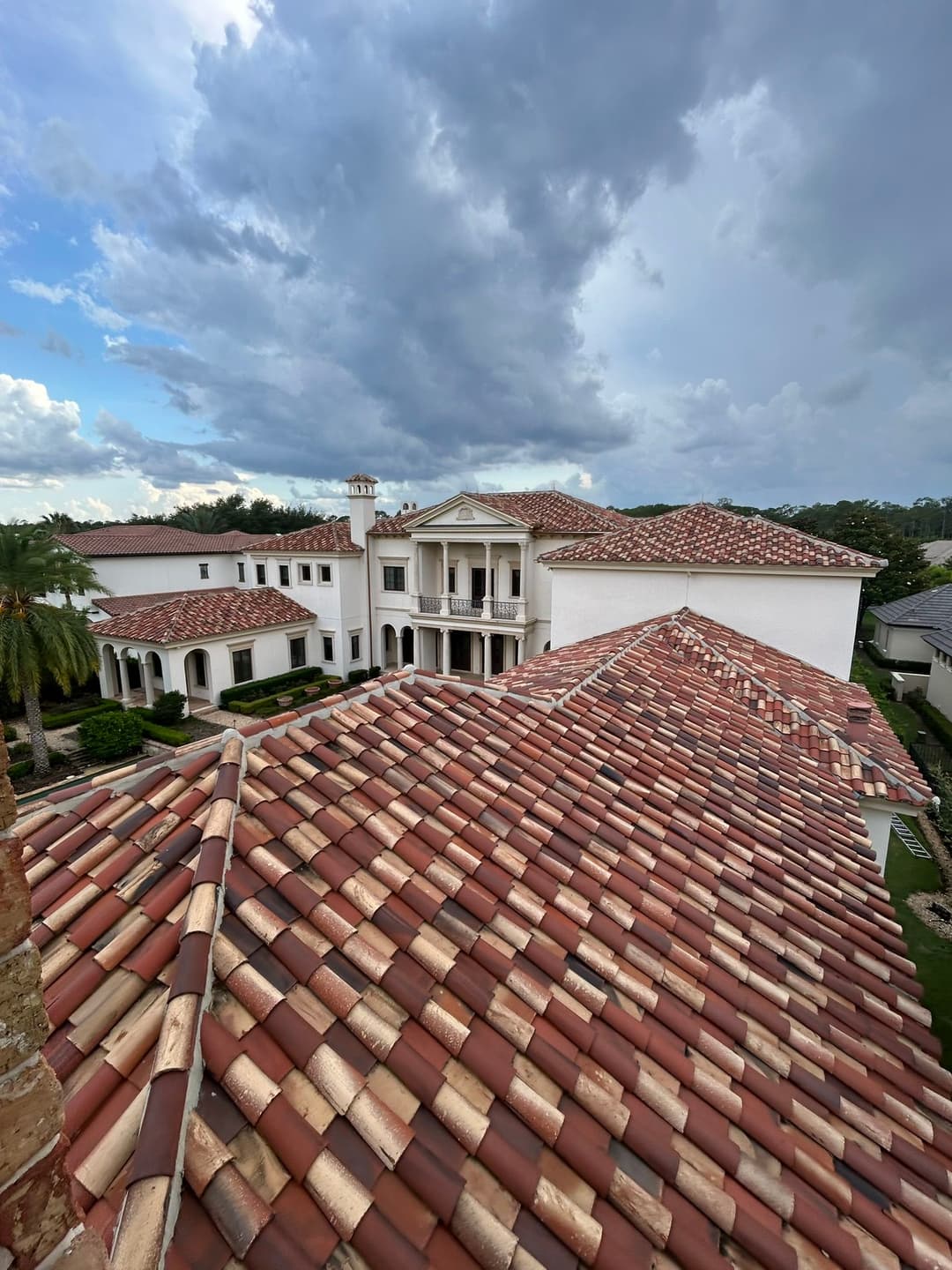Aerial view of a luxury Mediterranean-style villa with red tile roof under a cloudy sky.