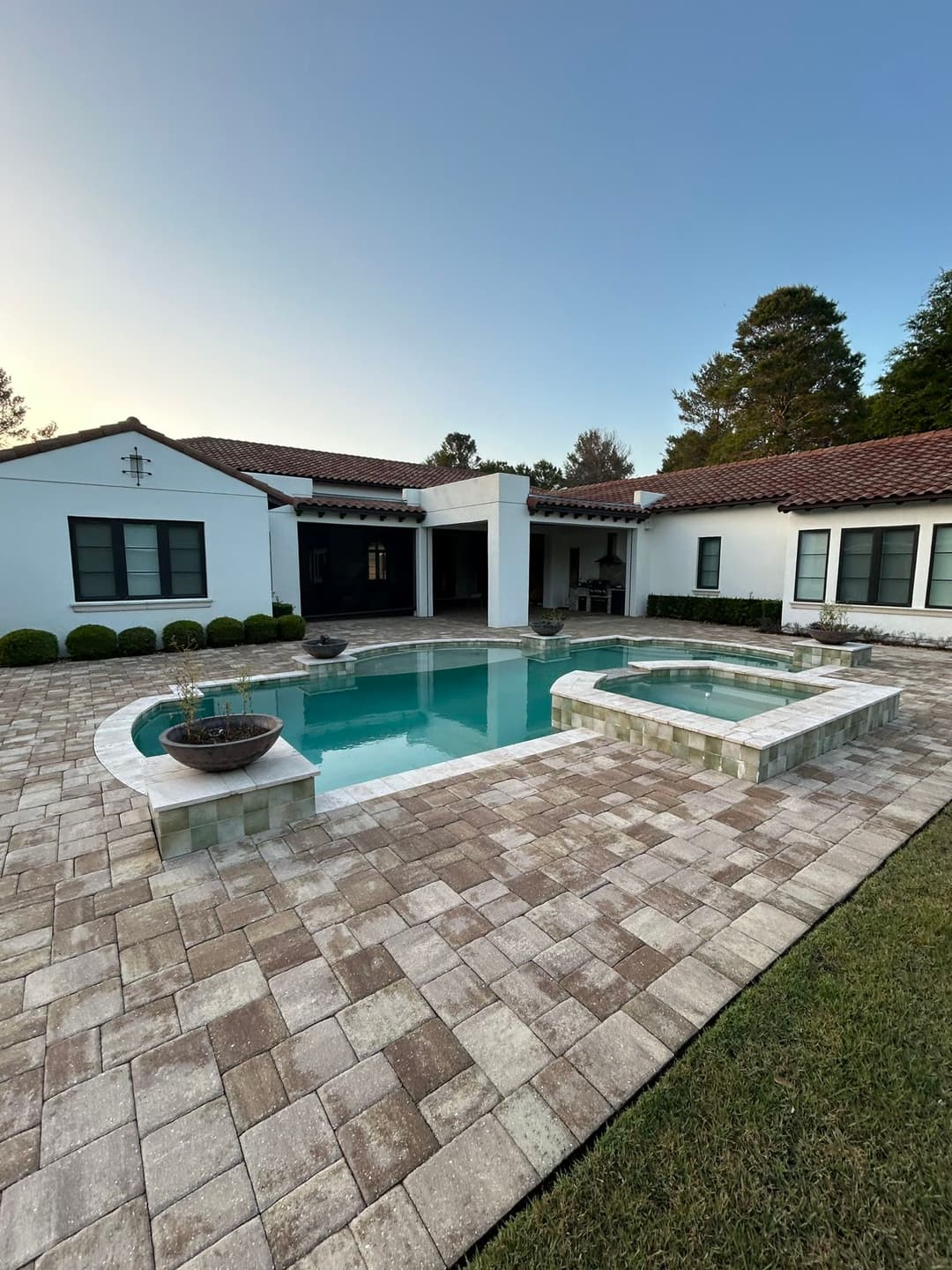 Modern home exterior with a pool and spa surrounded by stone pavers and lush landscaping.