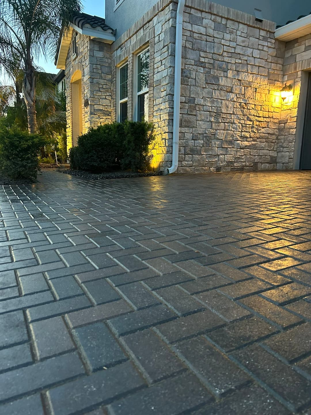 Paved driveway with stone texture, illuminated by outdoor lighting and adjacent shrubs.