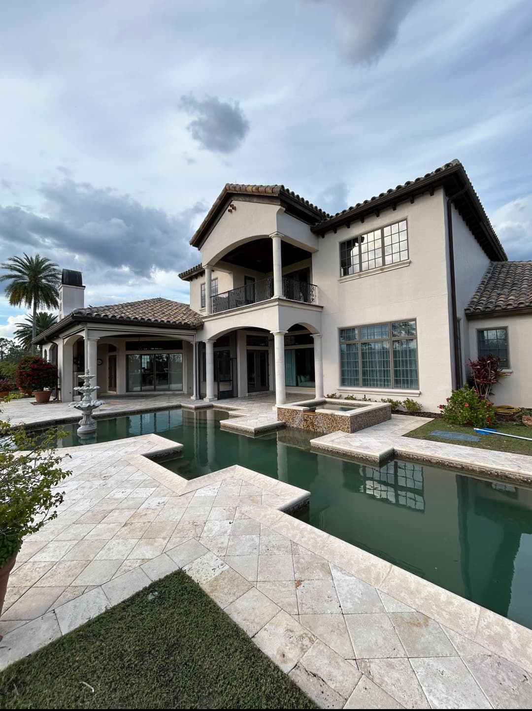 Luxury home with a pool and landscaped garden under a cloudy sky. Elegant architecture and design.