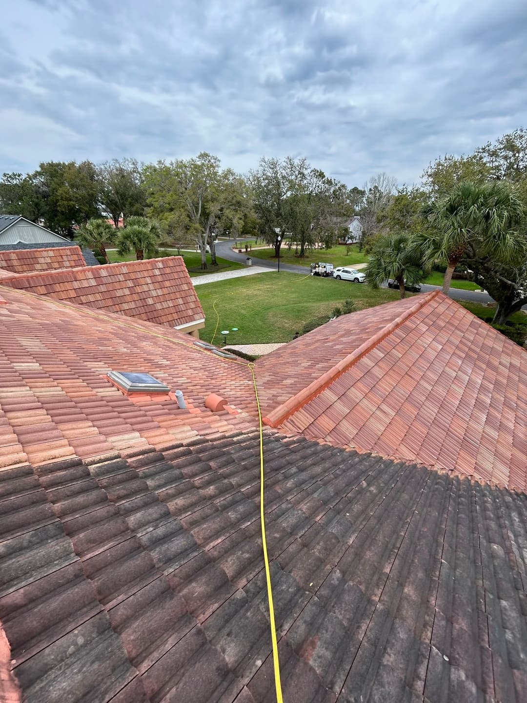 Aerial view of roof with red tiles, measuring tape on sloped area, and green lawn below.