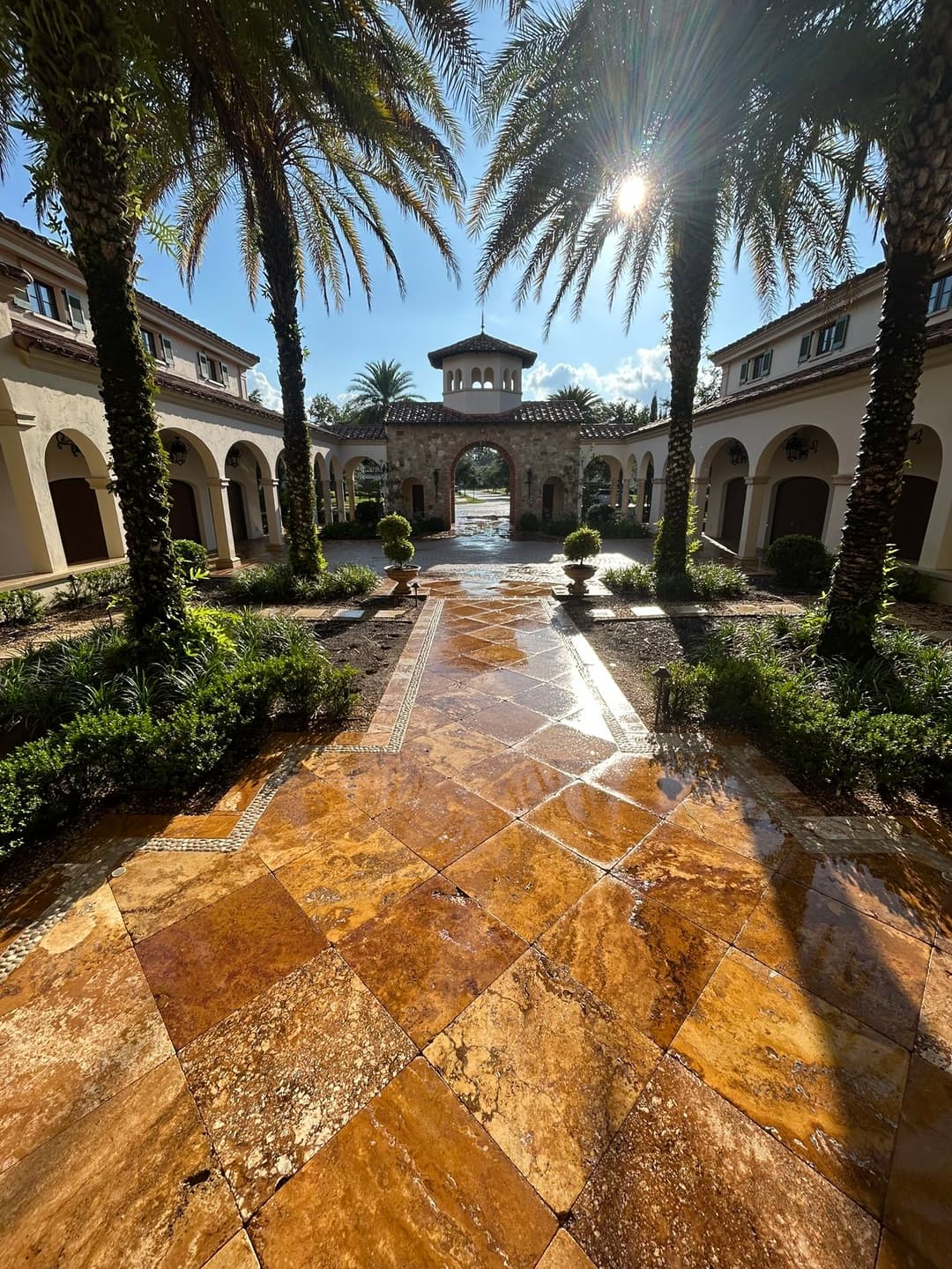 Tropical courtyard with palm trees, shining pathway, and beautiful architecture under sunlight.