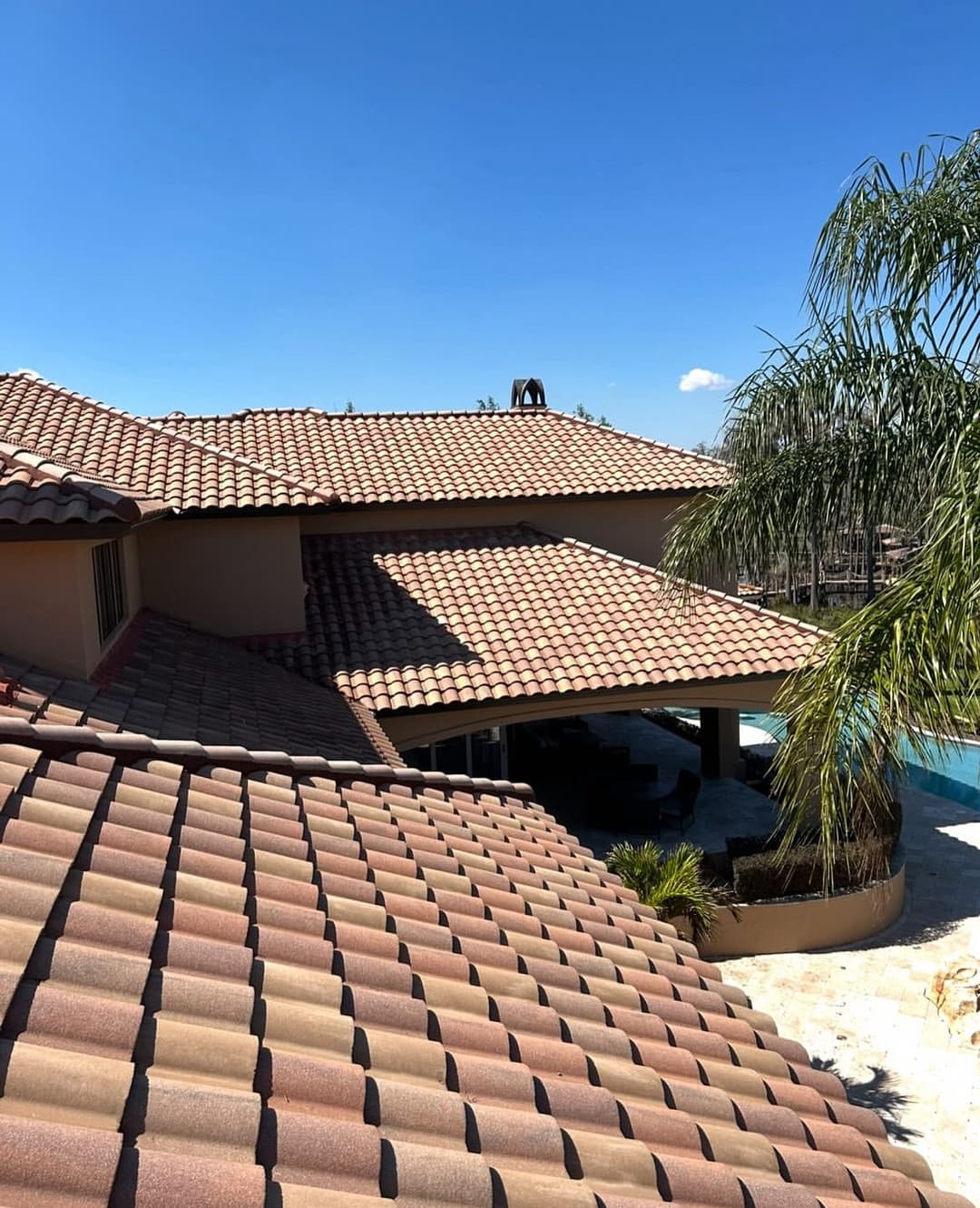View of a modern home with a terracotta tile roof and palm tree under a clear blue sky.