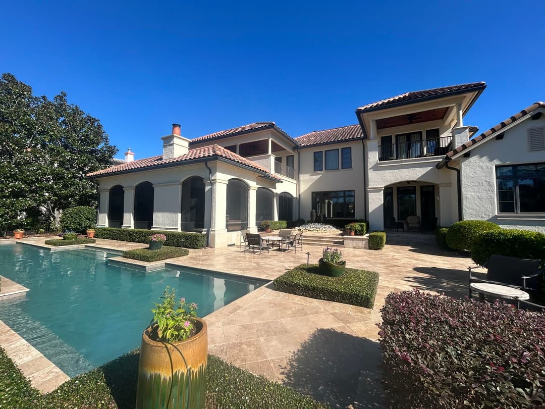 Luxury home with pool, manicured gardens, and outdoor seating under a clear blue sky.