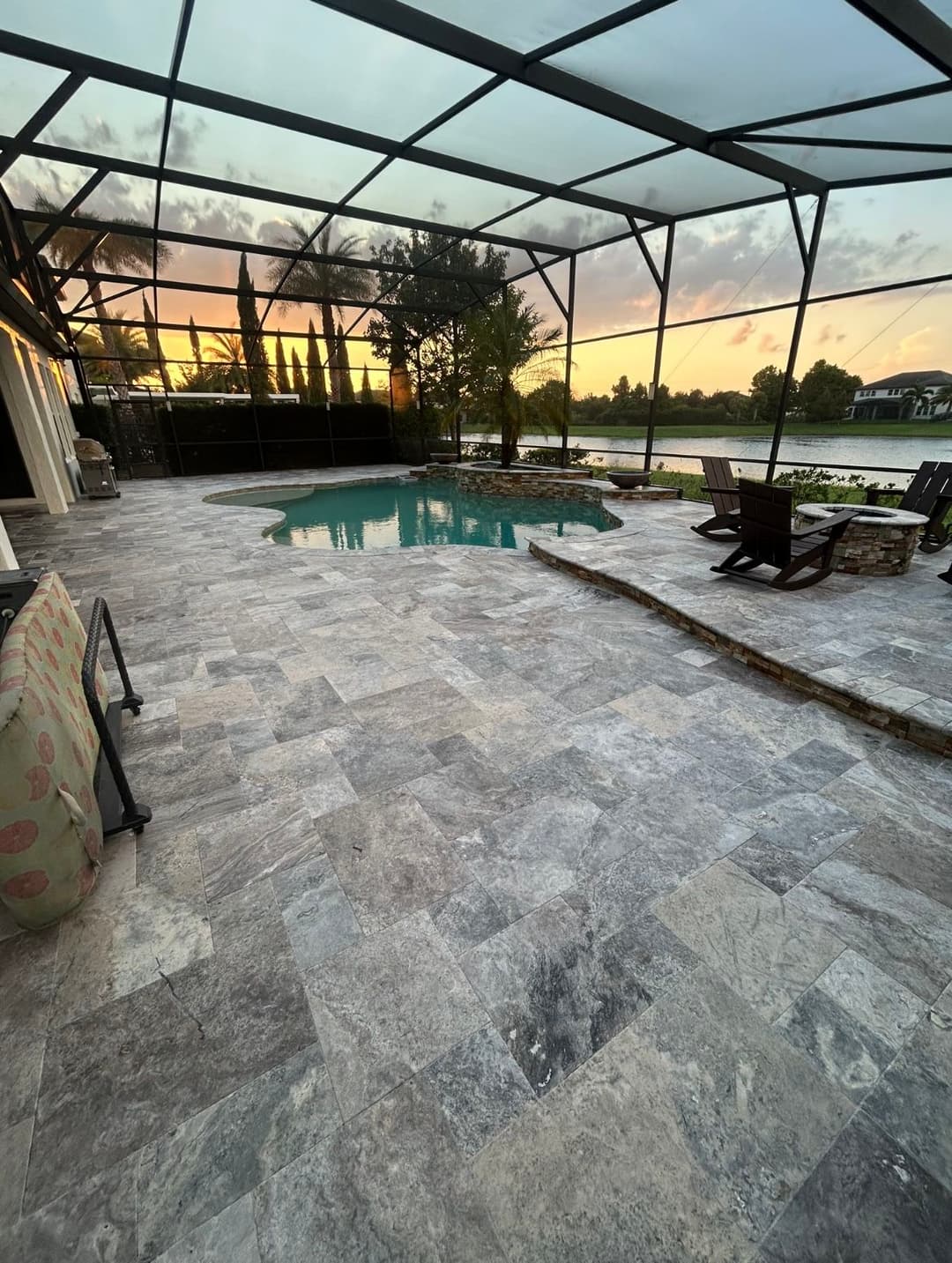 Elegant outdoor pool area with stone patio, surrounded by trees and a sunset view.