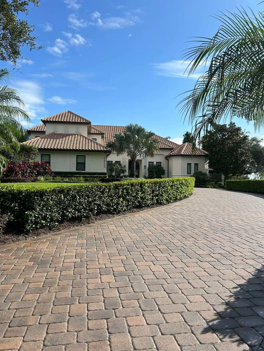 Elegant suburban home with a tiled roof surrounded by lush landscaping and a paved driveway.