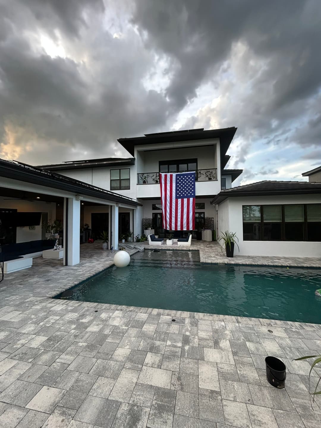 Modern home with American flag, pool, and cloud-filled sky. Ideal for outdoor living.