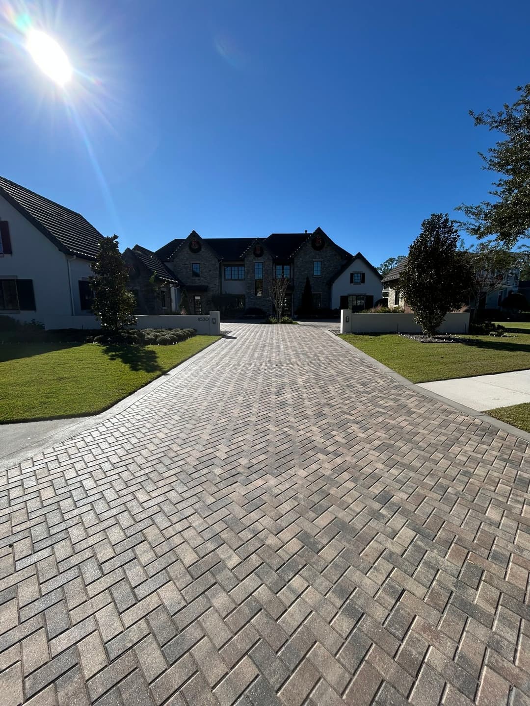 Paved driveway leading to a beautiful home under a clear blue sky. Sun shining brightly.